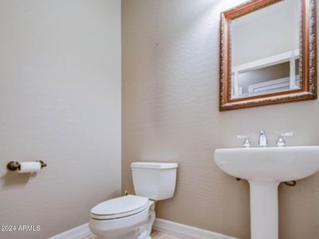 half bath featuring toilet, baseboards, and a sink