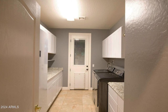 laundry area featuring light tile patterned flooring, washing machine and dryer, cabinets, and a textured ceiling