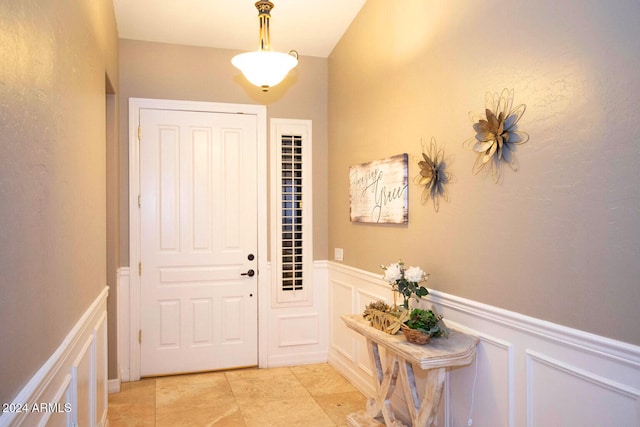 entryway with light tile patterned flooring, a decorative wall, and wainscoting