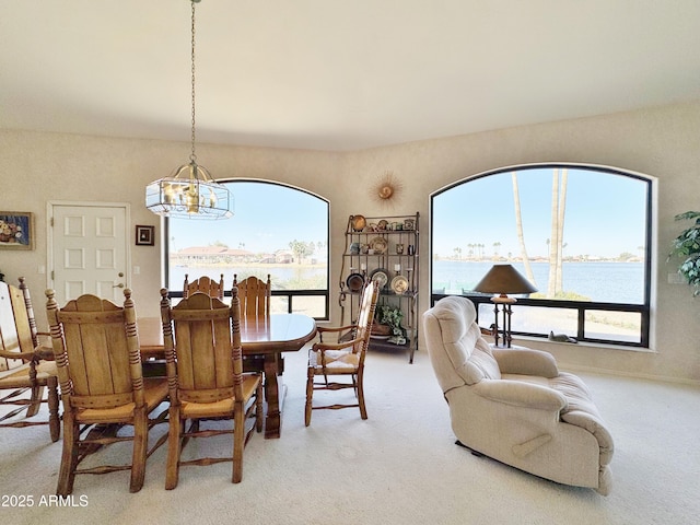 dining area featuring light carpet, a water view, and a notable chandelier