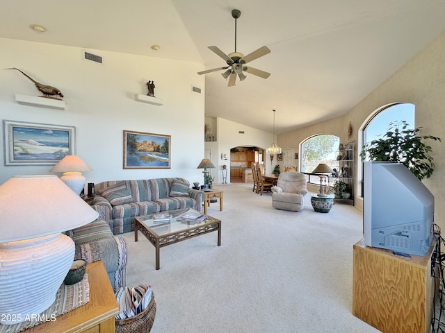 carpeted living room with high vaulted ceiling, arched walkways, visible vents, and ceiling fan with notable chandelier