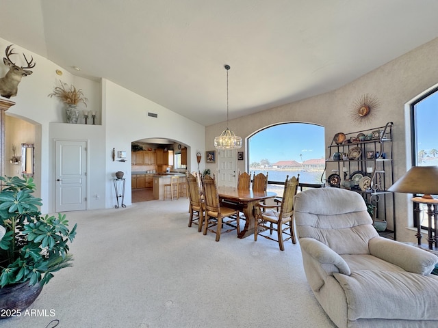 dining room with visible vents, arched walkways, light colored carpet, a water view, and an inviting chandelier