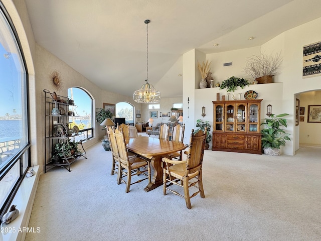 dining space featuring light carpet, high vaulted ceiling, arched walkways, and an inviting chandelier