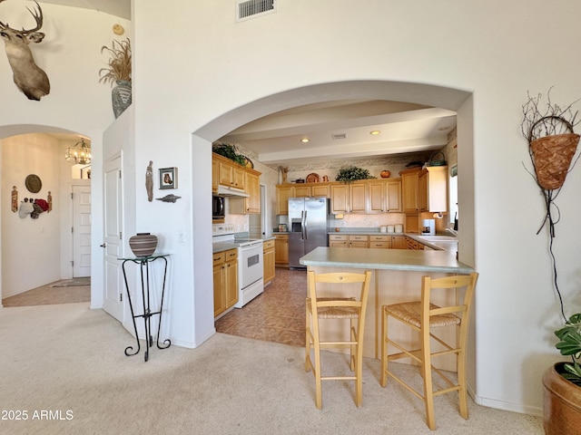 kitchen with arched walkways, white range with electric cooktop, light colored carpet, visible vents, and stainless steel fridge