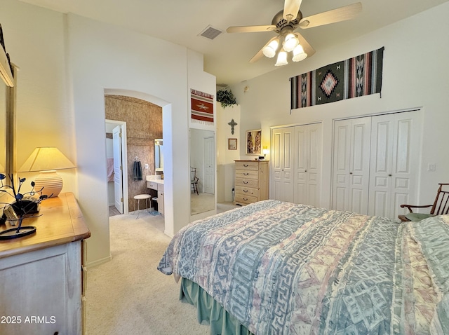 bedroom featuring light carpet, visible vents, arched walkways, a high ceiling, and multiple closets