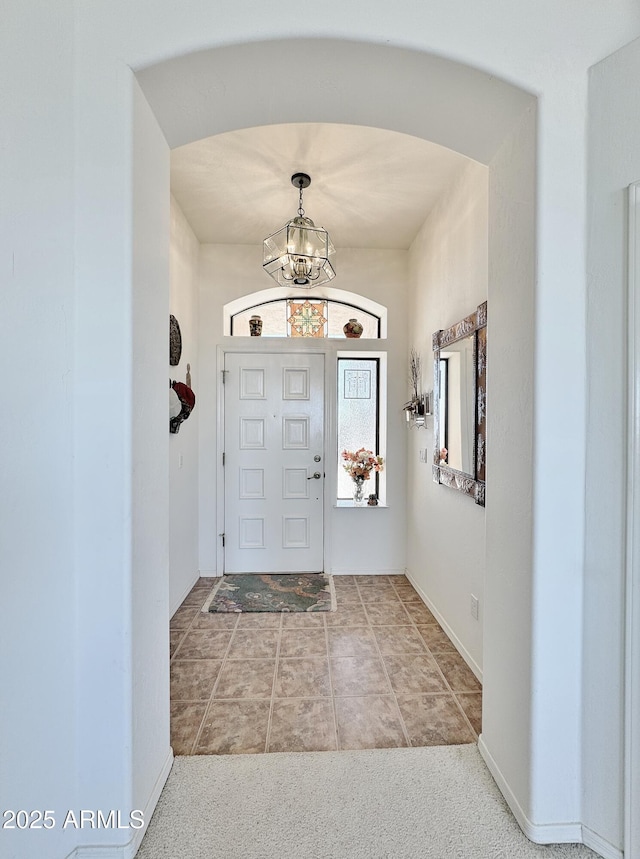 foyer with arched walkways, a notable chandelier, and baseboards