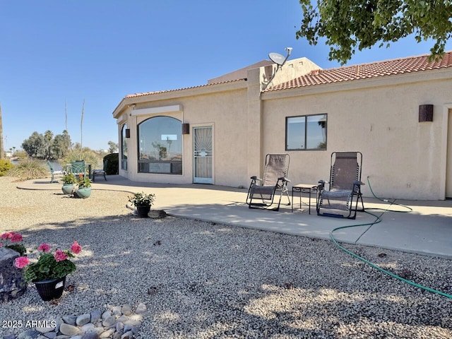 back of property with a tile roof, a patio area, and stucco siding