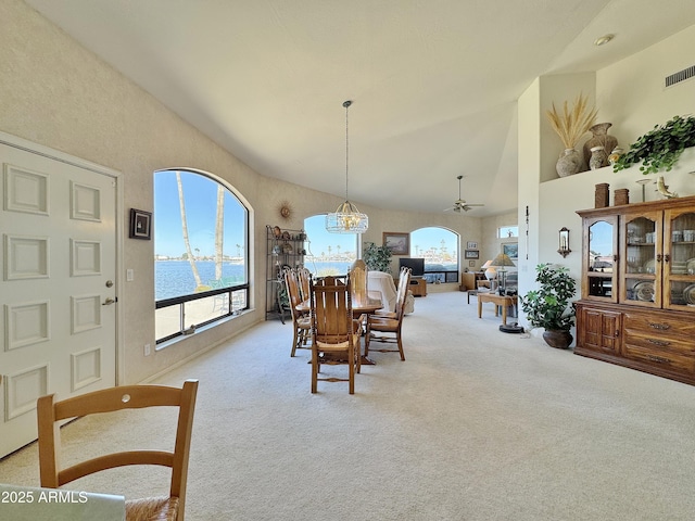 carpeted dining space with high vaulted ceiling, visible vents, and ceiling fan with notable chandelier