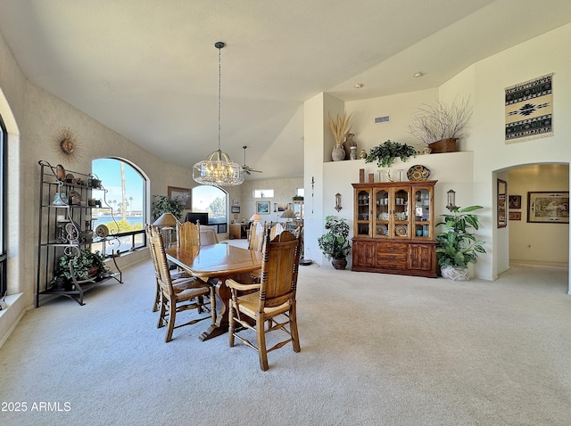 dining room with high vaulted ceiling, arched walkways, and light colored carpet