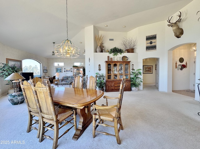 dining room with a high ceiling, arched walkways, a notable chandelier, and light colored carpet