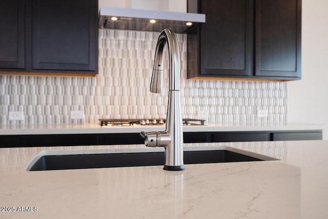 kitchen featuring light stone countertops, backsplash, and range hood