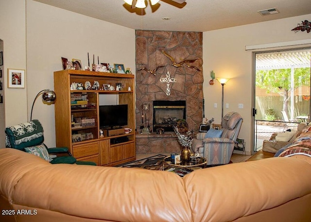 living room with a stone fireplace and ceiling fan