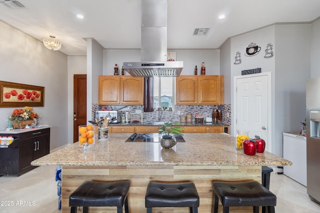 kitchen with island exhaust hood, visible vents, a breakfast bar area, and a center island