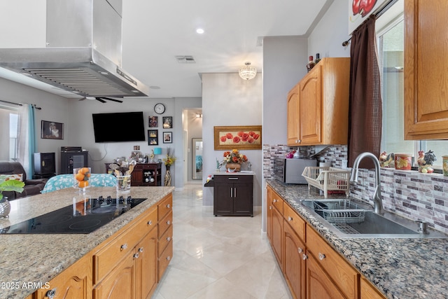 kitchen featuring island exhaust hood, visible vents, a sink, light stone countertops, and black electric cooktop