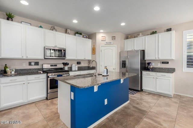 kitchen with a kitchen island with sink, dark stone counters, white cabinets, sink, and stainless steel appliances