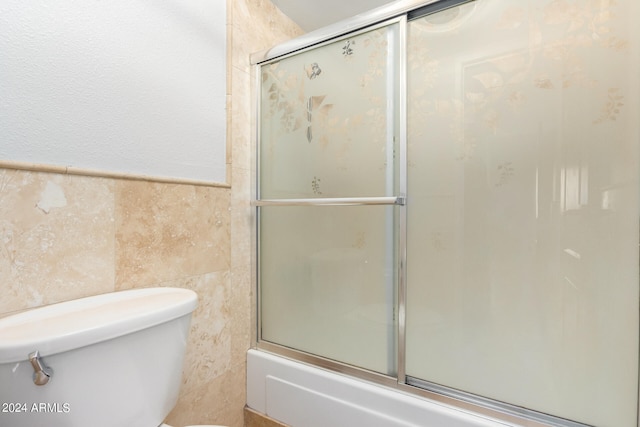 bathroom featuring combined bath / shower with glass door, tile walls, and toilet