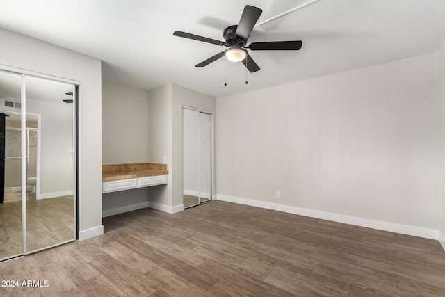 unfurnished bedroom featuring hardwood / wood-style flooring, two closets, and ceiling fan