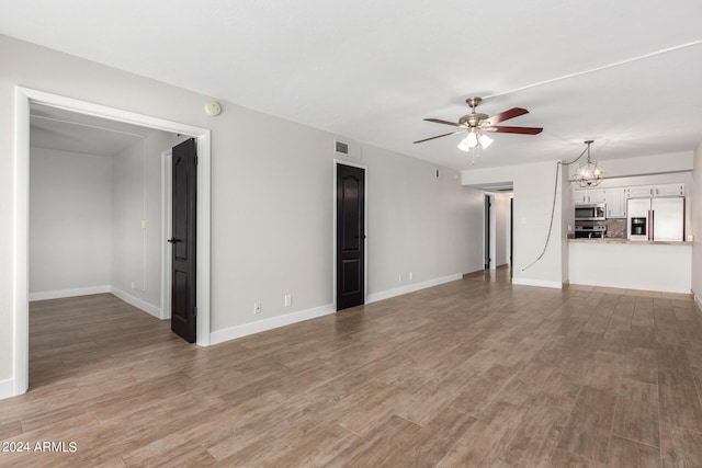 spare room with ceiling fan with notable chandelier and wood-type flooring