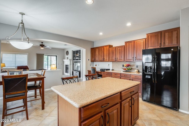 17562 W Agave Ct, Goodyear, AZ 85338 - kitchen with black fridge with ice dispenser, ceiling fan, arched walkways, light tile patterned floors, and brown cabinetry