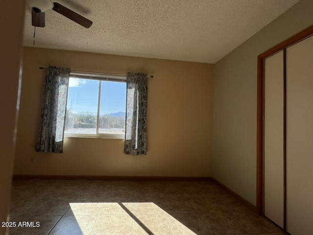 empty room featuring a textured ceiling, ceiling fan, and baseboards