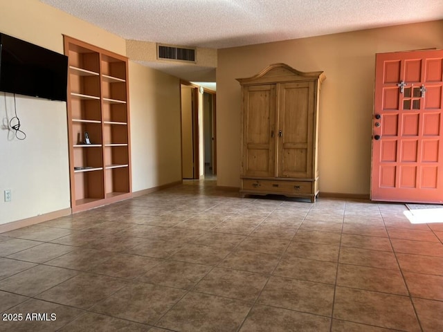 interior space featuring baseboards, visible vents, a textured ceiling, and dark tile patterned flooring