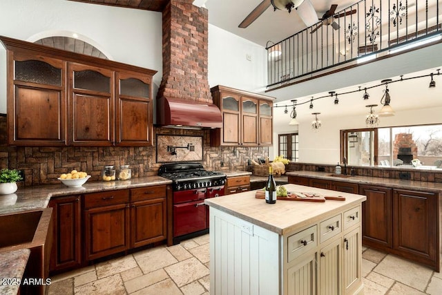 kitchen with a towering ceiling, sink, butcher block counters, ceiling fan, and wall chimney exhaust hood