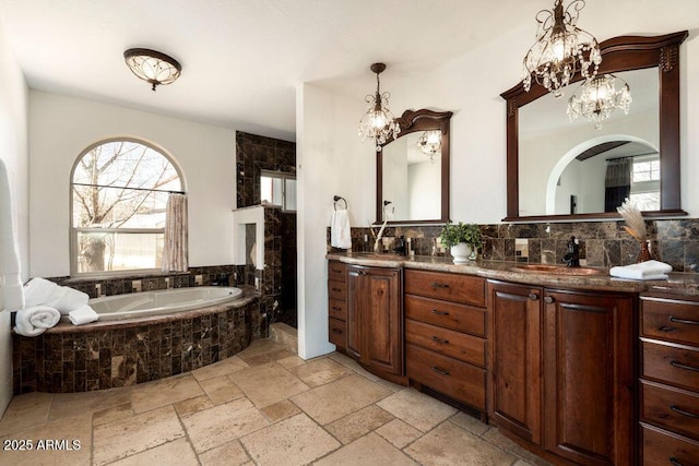 bathroom featuring an inviting chandelier, vanity, decorative backsplash, and tiled tub