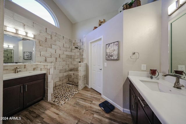 bathroom with hardwood / wood-style flooring, vanity, a tile shower, and vaulted ceiling