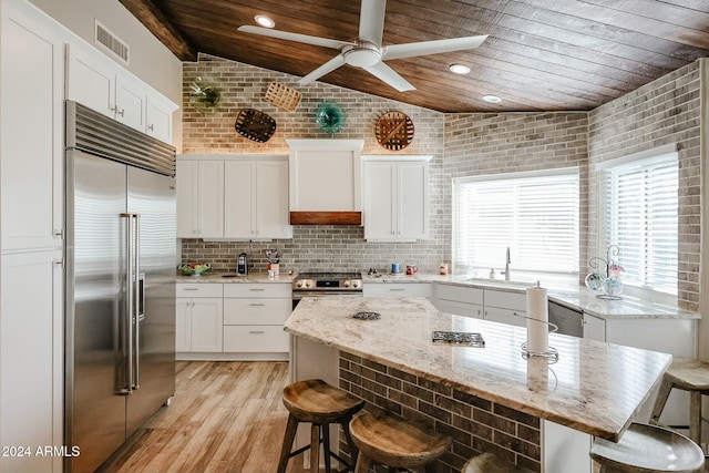 kitchen featuring a kitchen bar, custom range hood, stainless steel appliances, and vaulted ceiling