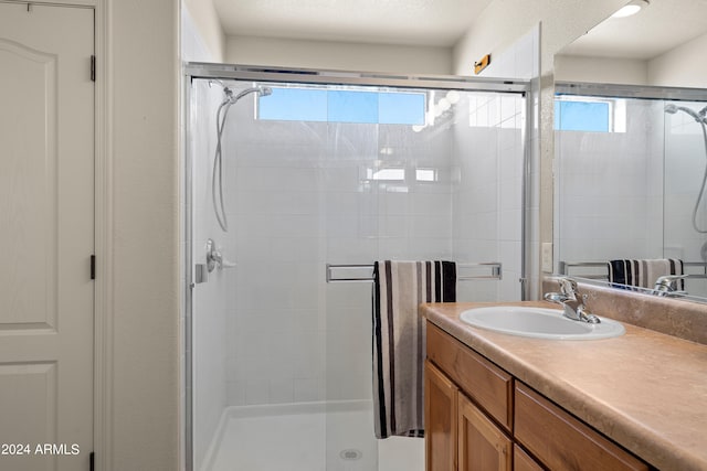 bathroom featuring plenty of natural light, a shower with door, a textured ceiling, and vanity