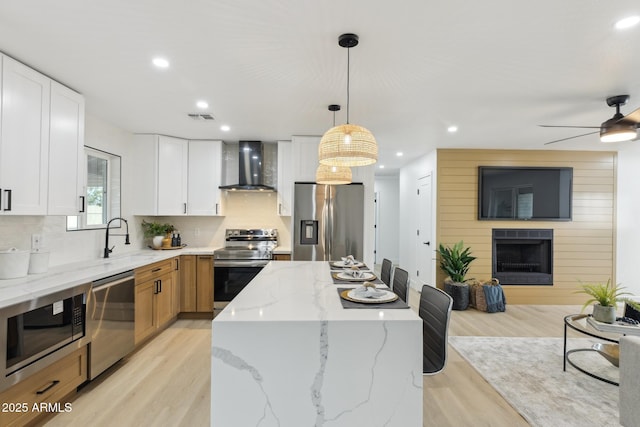 kitchen with a fireplace, stainless steel appliances, a sink, a kitchen island, and wall chimney exhaust hood