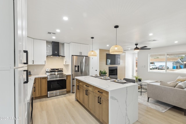 kitchen with wall chimney range hood, visible vents, stainless steel appliances, and open floor plan