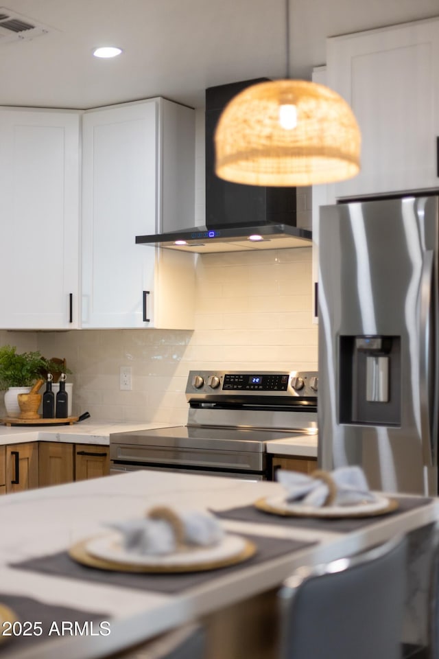 kitchen featuring decorative backsplash, stainless steel appliances, light countertops, wall chimney range hood, and white cabinetry