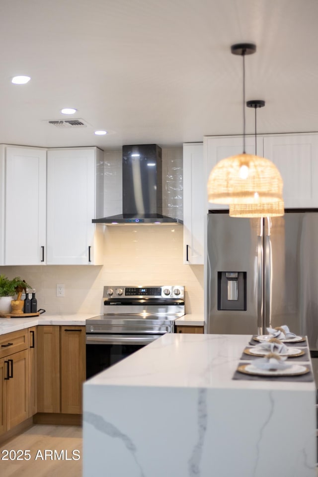 kitchen featuring tasteful backsplash, wall chimney exhaust hood, light stone countertops, stainless steel appliances, and white cabinetry