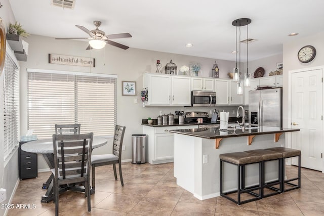 kitchen with visible vents, decorative light fixtures, a breakfast bar, white cabinets, and stainless steel appliances