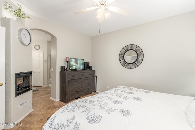 tiled bedroom featuring arched walkways, ceiling fan, a fireplace, and baseboards