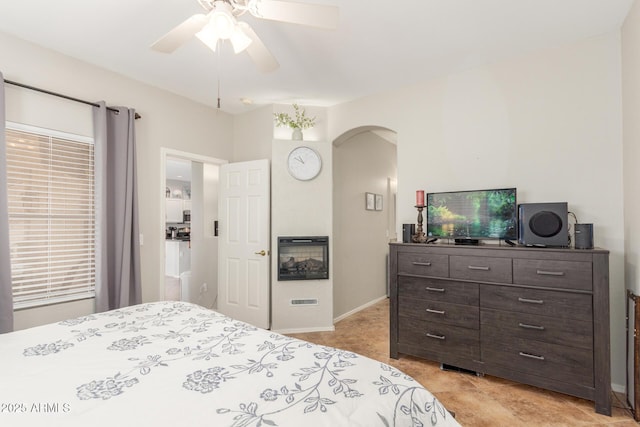 bedroom featuring arched walkways, a glass covered fireplace, a ceiling fan, and baseboards