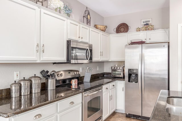 kitchen featuring white cabinets, stainless steel appliances, and dark stone counters