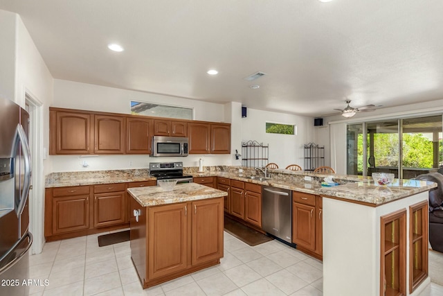 kitchen featuring kitchen peninsula, light stone counters, stainless steel appliances, ceiling fan, and a center island