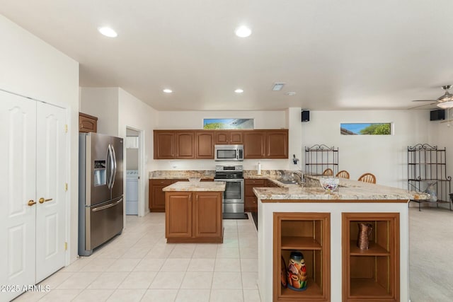 kitchen with light stone countertops, appliances with stainless steel finishes, ceiling fan, sink, and an island with sink