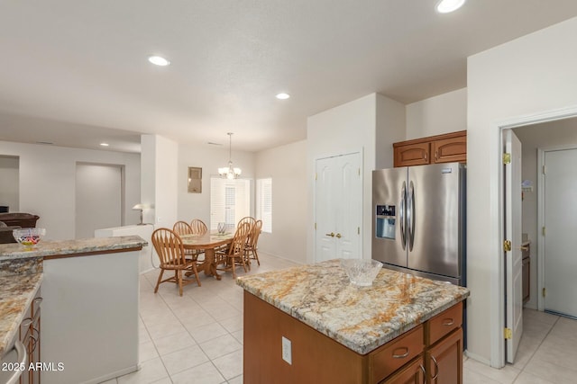 kitchen featuring light stone countertops, hanging light fixtures, an inviting chandelier, stainless steel refrigerator with ice dispenser, and a kitchen island