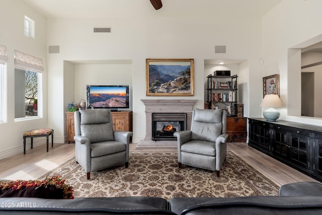 living area featuring a high ceiling, visible vents, wood finished floors, and a glass covered fireplace