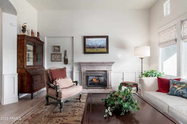 living area with arched walkways, a decorative wall, wood finished floors, wainscoting, and a glass covered fireplace