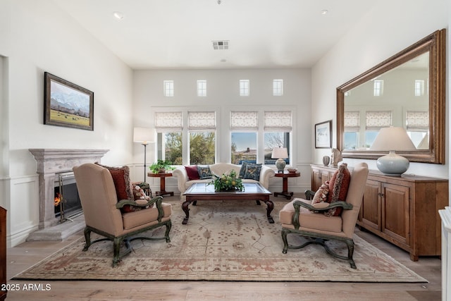 sitting room featuring a lit fireplace, a high ceiling, wood finished floors, and visible vents