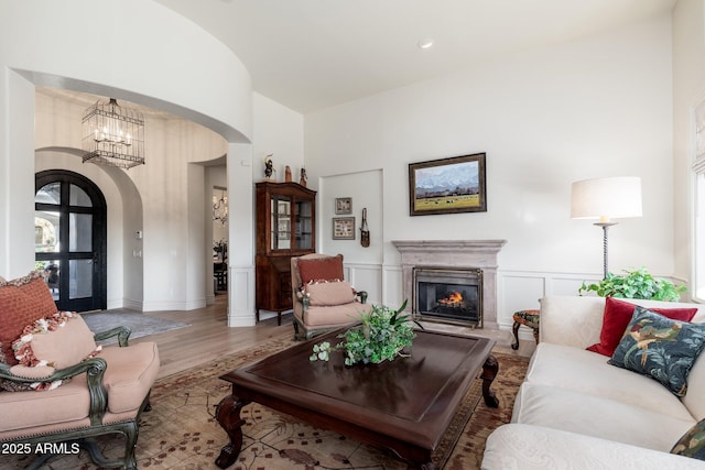 living room with arched walkways, a decorative wall, a glass covered fireplace, wainscoting, and wood finished floors