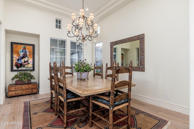 dining area with a raised ceiling, baseboards, a notable chandelier, and light wood finished floors