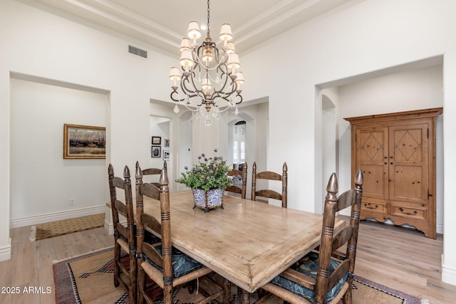 dining space with visible vents, arched walkways, a raised ceiling, light wood-style flooring, and a chandelier