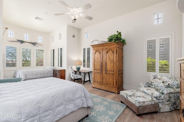 bedroom with light wood-style floors, visible vents, a high ceiling, and multiple windows