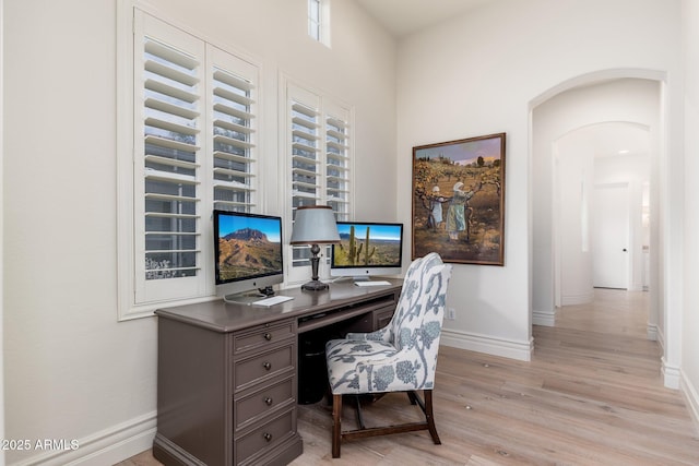 home office featuring arched walkways, baseboards, and light wood finished floors