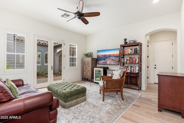 living room with arched walkways, visible vents, light wood-style flooring, a ceiling fan, and baseboards